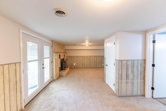 carpeted empty room with french doors, a wood stove, and wood walls