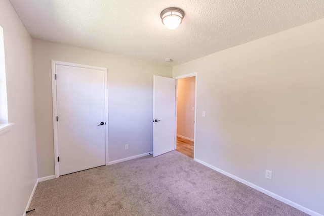 unfurnished bedroom featuring light colored carpet, a textured ceiling, and a closet