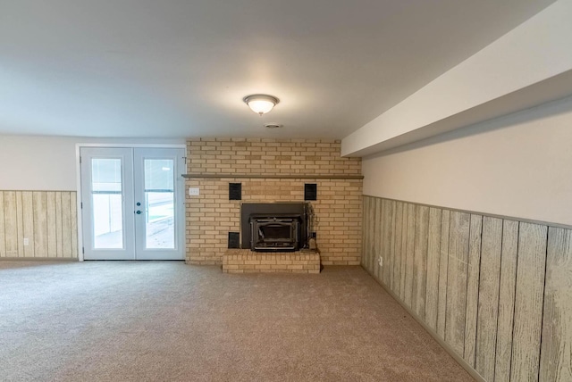 unfurnished living room with a wood stove, wooden walls, french doors, and light colored carpet