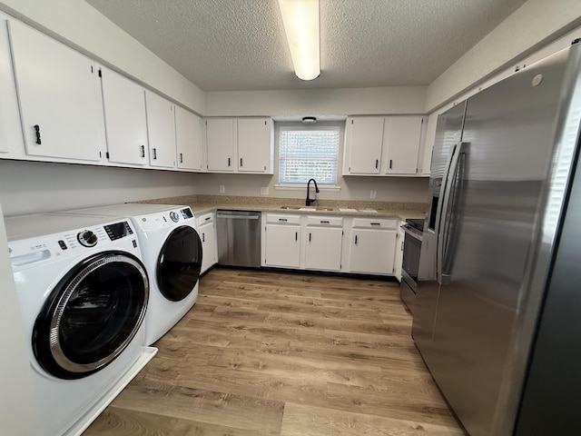 laundry area with washer and clothes dryer, light wood finished floors, a textured ceiling, and a sink