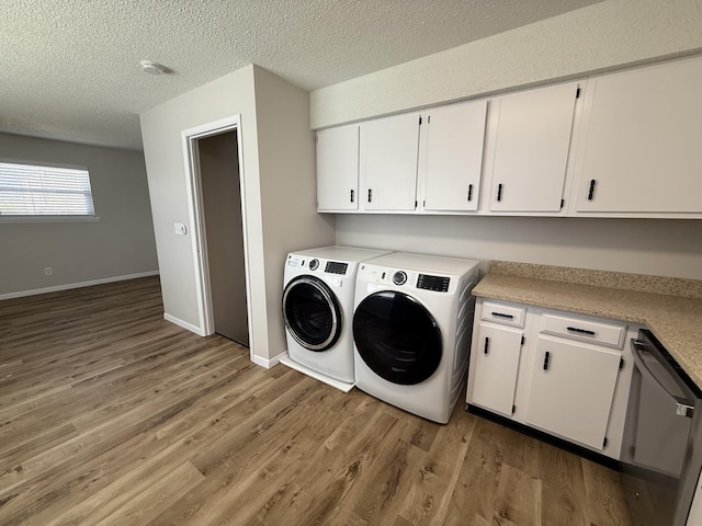 laundry area featuring a textured ceiling, cabinet space, separate washer and dryer, and light wood finished floors