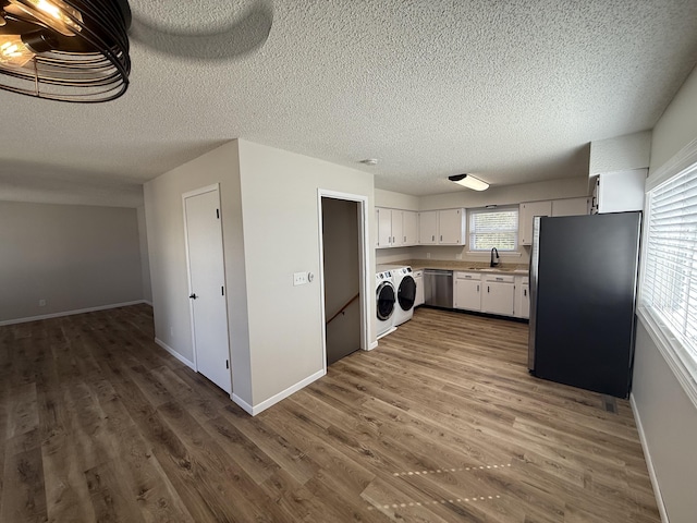 kitchen featuring washing machine and dryer, wood finished floors, white cabinets, stainless steel appliances, and a sink