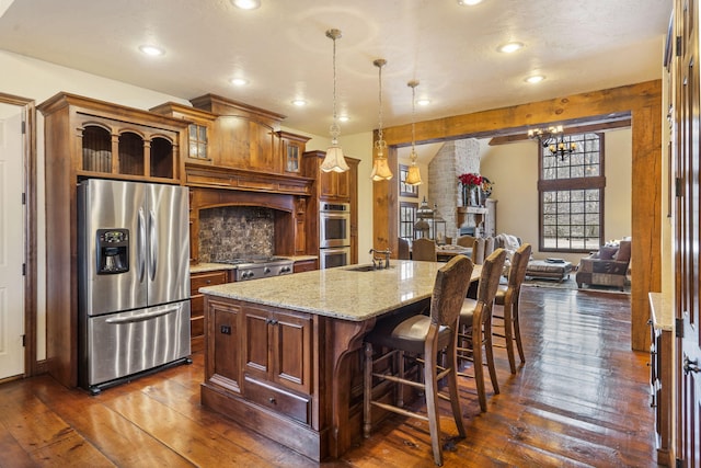 kitchen featuring light stone countertops, dark hardwood / wood-style flooring, decorative light fixtures, a center island with sink, and appliances with stainless steel finishes