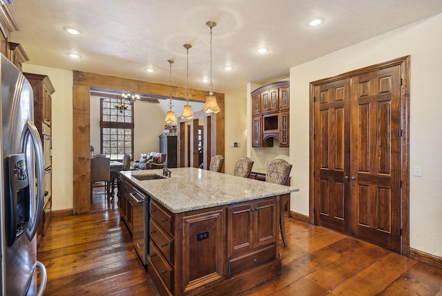 kitchen featuring pendant lighting, a center island with sink, dark hardwood / wood-style floors, stainless steel fridge, and light stone countertops