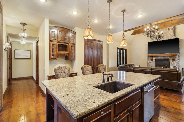 kitchen featuring a center island with sink, a stone fireplace, sink, hanging light fixtures, and light stone countertops