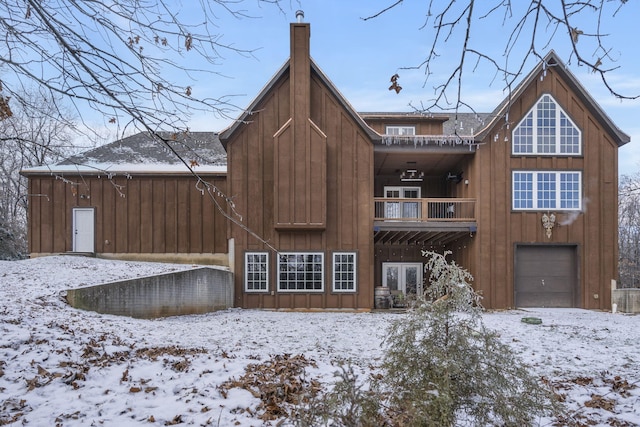 snow covered back of property featuring a balcony, french doors, and a garage