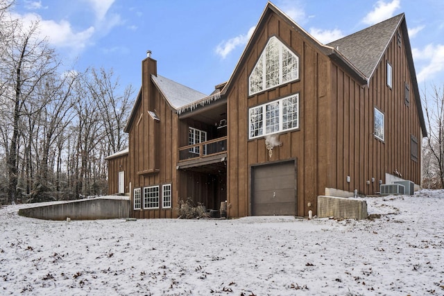 snow covered rear of property featuring a balcony, a garage, and cooling unit