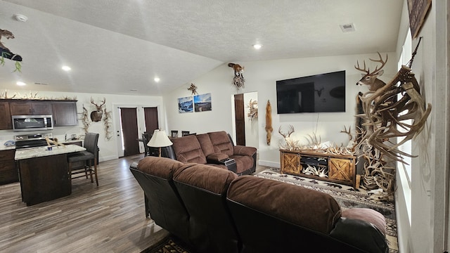 living area with wood finished floors, baseboards, visible vents, vaulted ceiling, and a textured ceiling