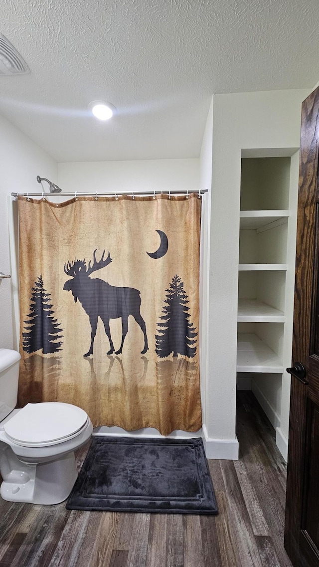 bathroom with hardwood / wood-style floors, built in shelves, toilet, and a textured ceiling