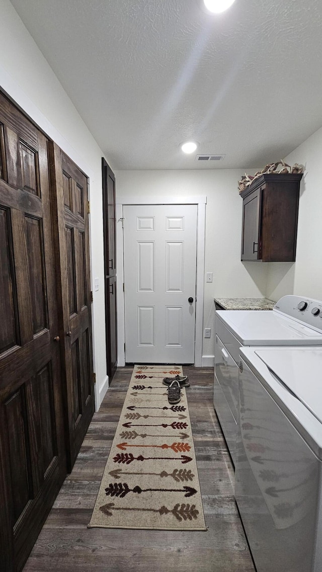 washroom with visible vents, a textured ceiling, cabinet space, dark wood-style flooring, and washing machine and clothes dryer