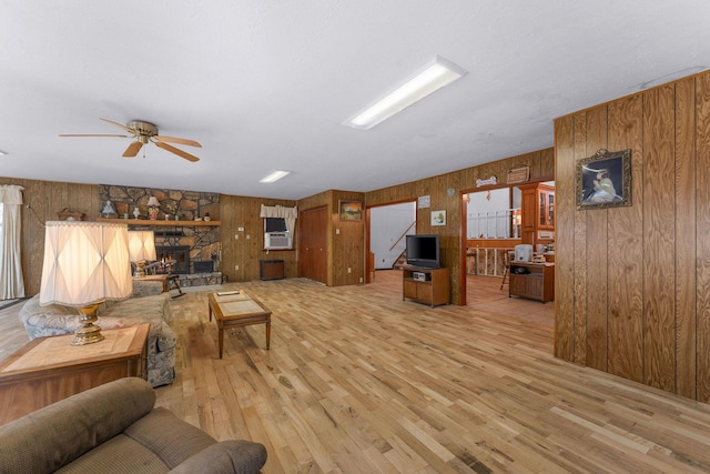 living area featuring light wood-style floors, a fireplace, wooden walls, and a ceiling fan