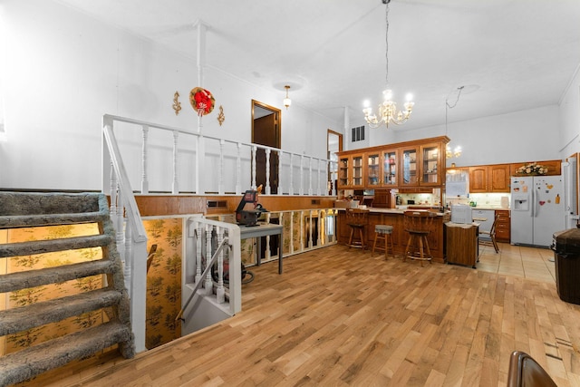 interior space with a breakfast bar, white refrigerator with ice dispenser, brown cabinets, light wood finished floors, and an inviting chandelier