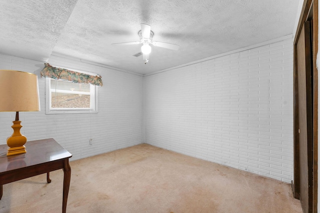 spare room with brick wall, a ceiling fan, a textured ceiling, and light colored carpet