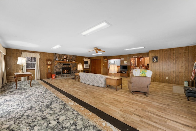 living room featuring wood walls, ceiling fan, a fireplace, and wood finished floors