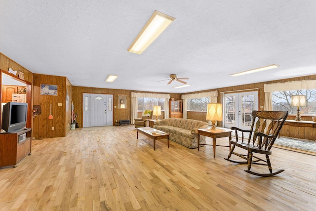 living area featuring light wood-style floors, french doors, a textured ceiling, and wooden walls