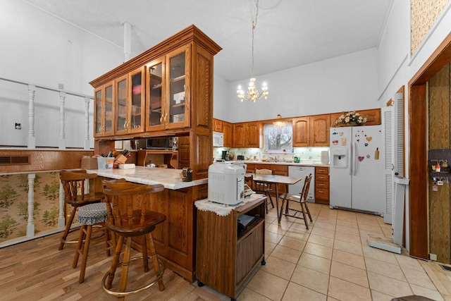 kitchen with a peninsula, white appliances, a high ceiling, and brown cabinetry