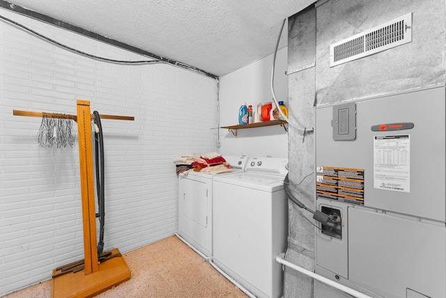 washroom featuring washing machine and clothes dryer, visible vents, a textured ceiling, brick wall, and laundry area