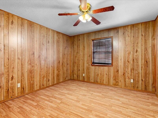 unfurnished room with ceiling fan, a textured ceiling, wooden walls, and light hardwood / wood-style flooring