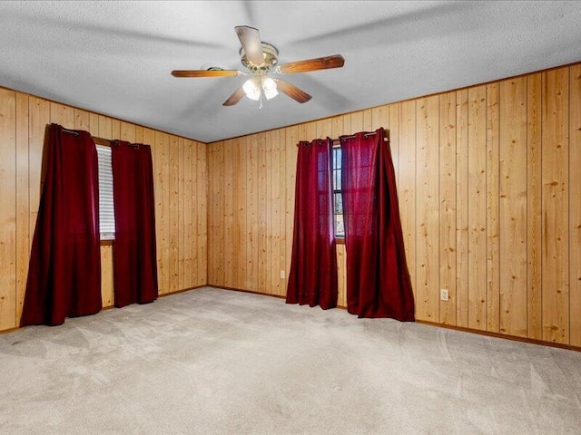 carpeted spare room with ceiling fan, wooden walls, and a textured ceiling