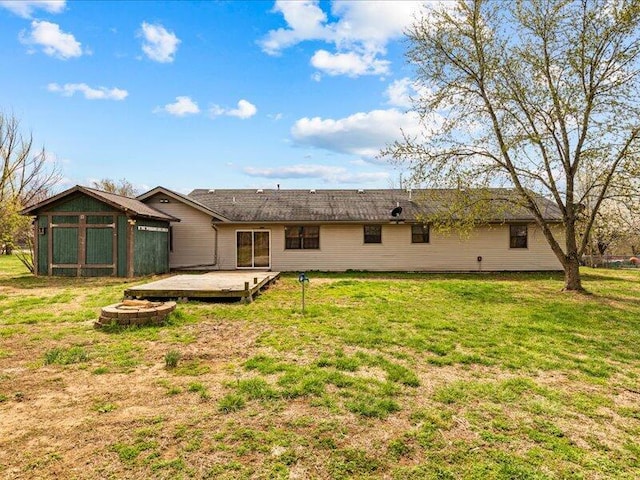 rear view of property featuring a shed, an outdoor fire pit, a deck, and a lawn