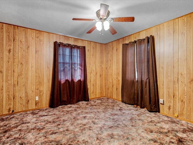 carpeted spare room with ceiling fan, wooden walls, and a textured ceiling