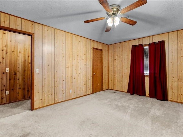 empty room with a textured ceiling, light colored carpet, ceiling fan, and wooden walls