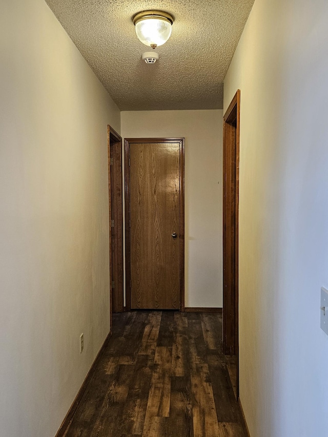 hall with a textured ceiling and dark wood-type flooring