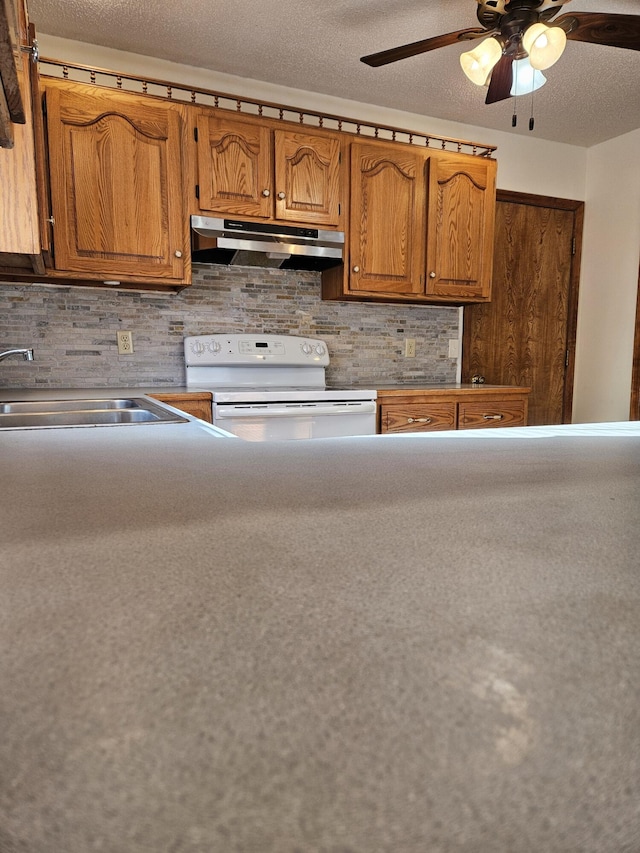 kitchen featuring ceiling fan, sink, backsplash, stove, and a textured ceiling