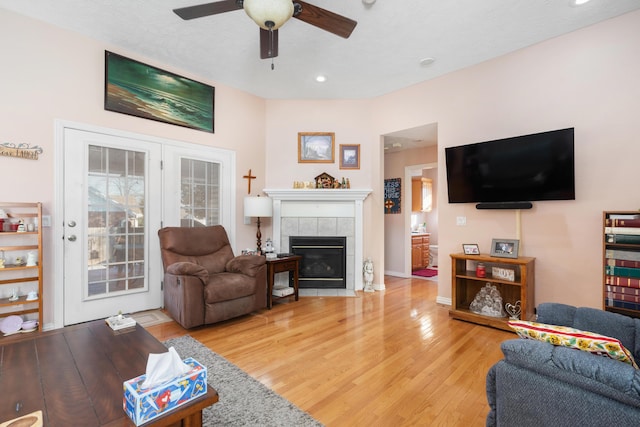 living room featuring ceiling fan, light hardwood / wood-style flooring, and a tiled fireplace