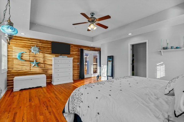 bedroom with ceiling fan, hardwood / wood-style floors, a raised ceiling, and wooden walls