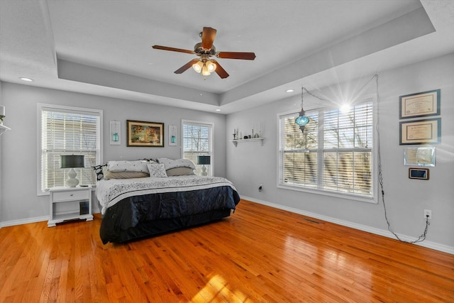 bedroom featuring light wood-type flooring, ceiling fan, and a tray ceiling