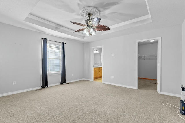 unfurnished bedroom featuring a spacious closet, ceiling fan, and a tray ceiling