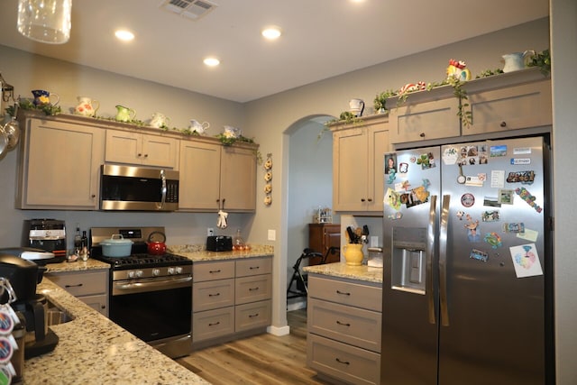 kitchen featuring light stone counters, pendant lighting, stainless steel appliances, and light hardwood / wood-style floors