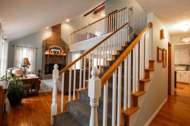 stairs featuring hardwood / wood-style flooring, vaulted ceiling, a brick fireplace, and a textured ceiling