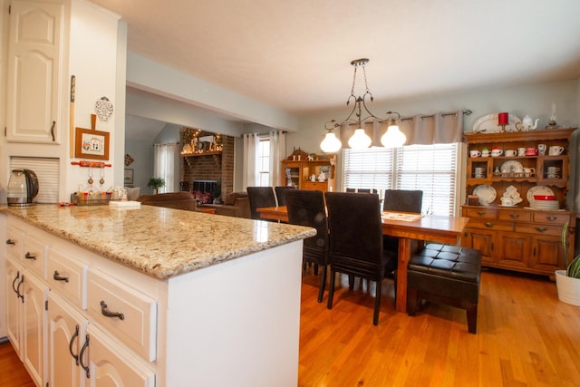 kitchen featuring pendant lighting, a fireplace, white cabinets, light stone counters, and light hardwood / wood-style flooring