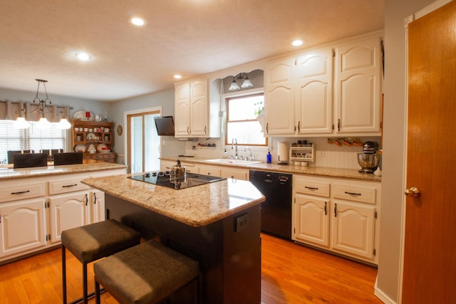 kitchen with sink, hanging light fixtures, a kitchen breakfast bar, a center island, and black appliances