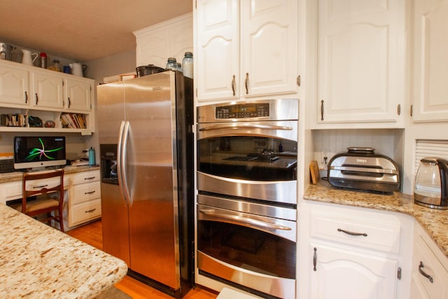 kitchen featuring stainless steel appliances, light stone countertops, white cabinets, and light hardwood / wood-style floors