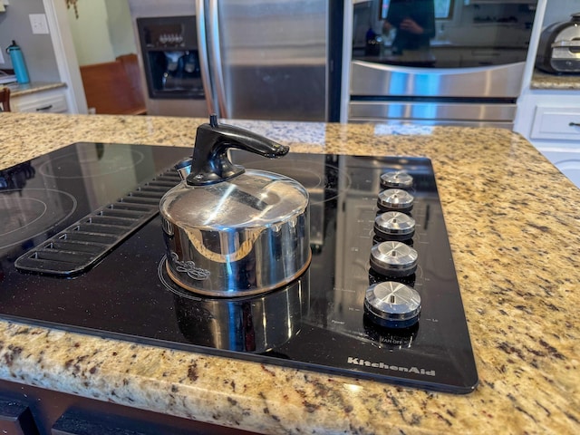 interior details featuring black electric cooktop, light stone countertops, and stainless steel fridge with ice dispenser