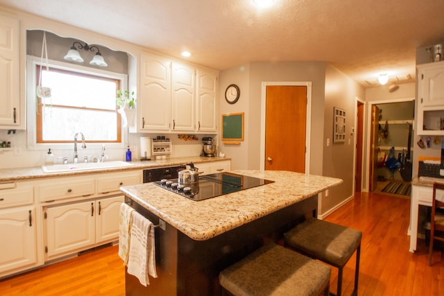 kitchen featuring sink, hardwood / wood-style flooring, white cabinetry, a center island, and black electric cooktop