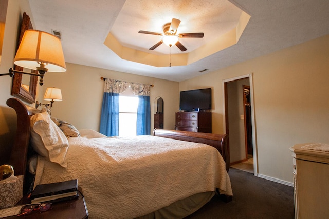 bedroom featuring dark colored carpet, a spacious closet, ceiling fan, and a tray ceiling