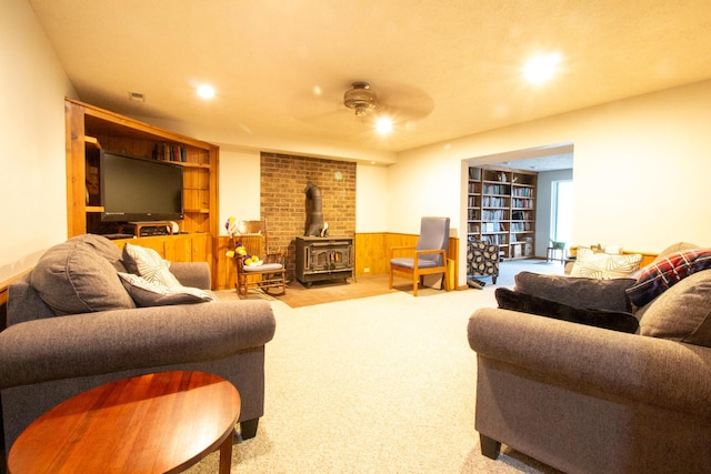 carpeted living room featuring built in shelves, a wood stove, ceiling fan, and wood walls