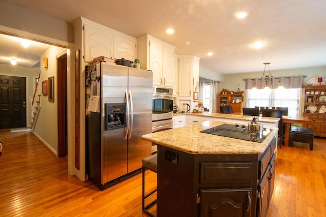 kitchen featuring a breakfast bar, appliances with stainless steel finishes, a center island, a notable chandelier, and white cabinets