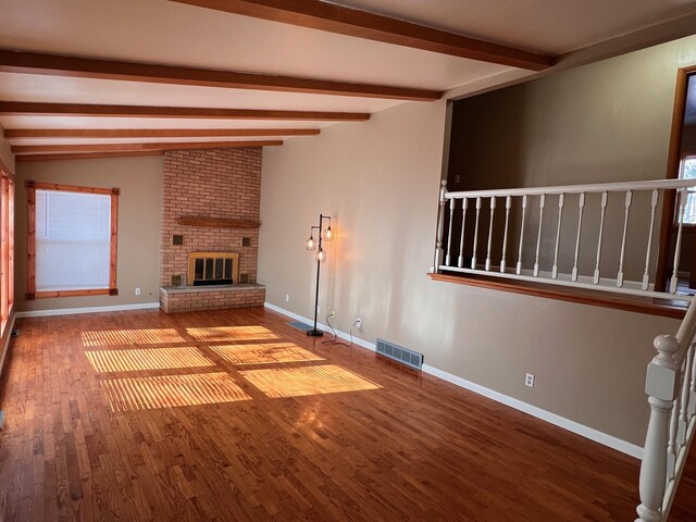 unfurnished living room featuring hardwood / wood-style floors, lofted ceiling with beams, and a brick fireplace