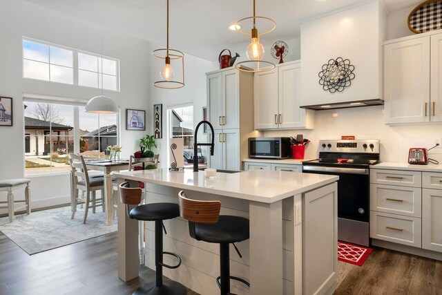 kitchen featuring a kitchen island with sink, white cabinets, stainless steel appliances, and decorative light fixtures