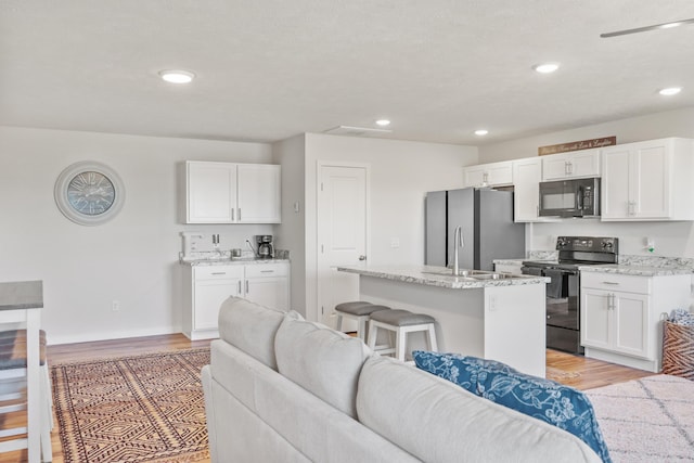 kitchen featuring a kitchen bar, an island with sink, white cabinets, light stone counters, and black appliances