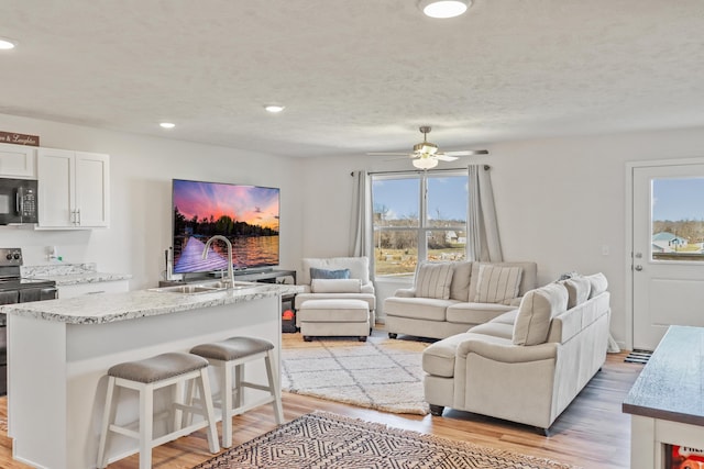 living room with light hardwood / wood-style floors, sink, a textured ceiling, and ceiling fan