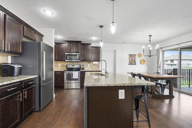 kitchen featuring a breakfast bar, stainless steel appliances, dark brown cabinets, backsplash, and a sink