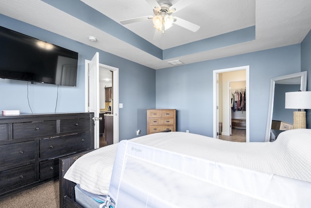 bedroom featuring a raised ceiling, visible vents, a ceiling fan, ensuite bath, and a walk in closet