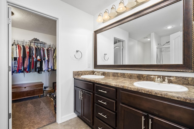 bathroom with double vanity, a shower with shower door, a spacious closet, and a sink