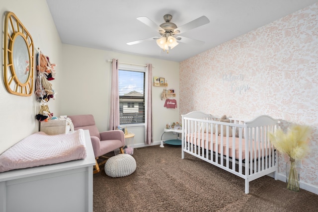carpeted bedroom with baseboards, a crib, a ceiling fan, and wallpapered walls